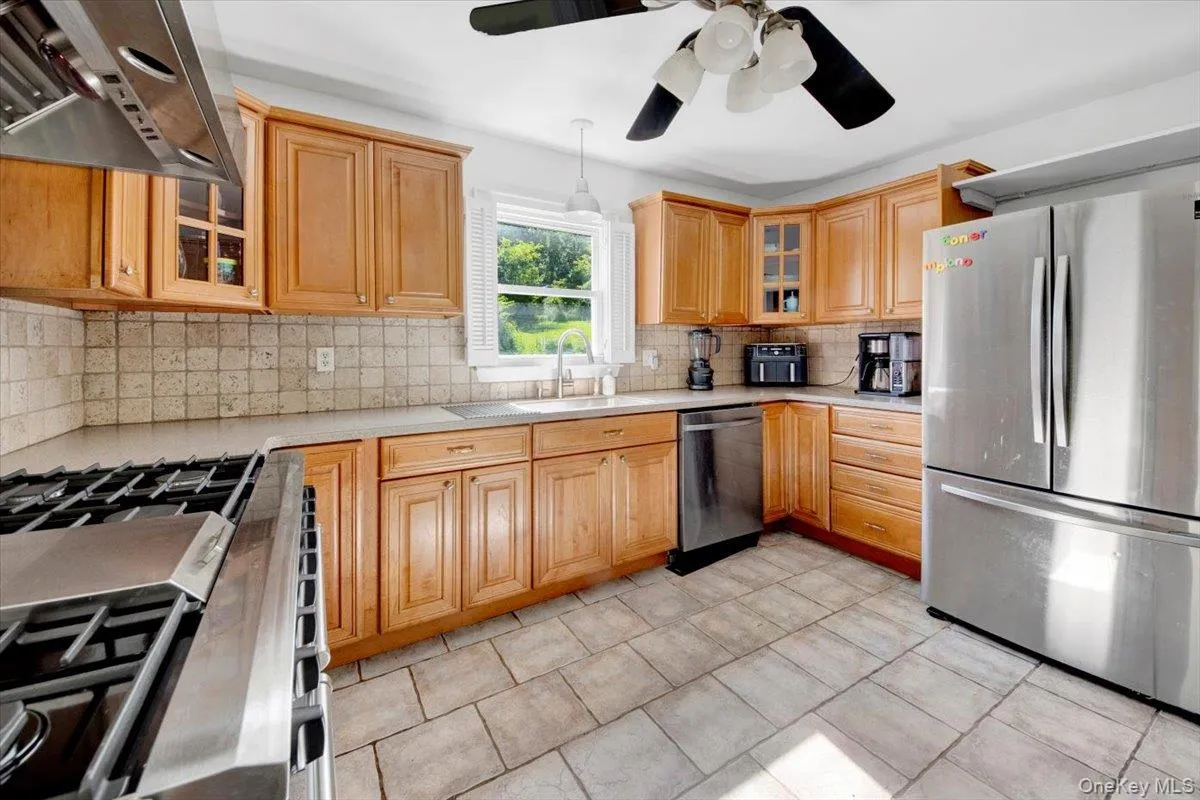 Kitchen featuring glass insert cabinets, appliances with stainless steel finishes, wall chimney exhaust hood, and decorative backsplash Kitchen featuring glass insert cabinets, appliances with stainless steel finishes, wall chimney exhaust hood, and decorative backsplash
