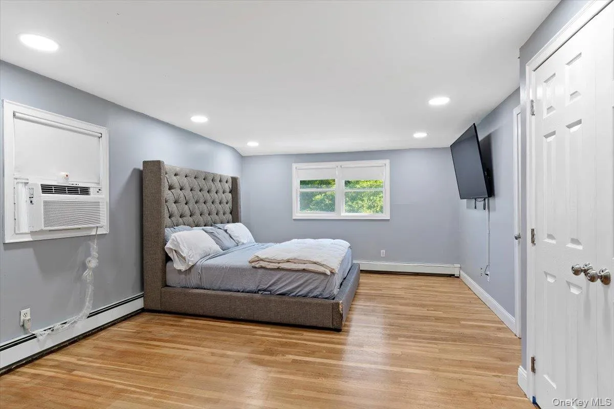Primary Bedroom featuring light wood-style floors, recessed lighting, a baseboard heating unit, and cooling unit Primary Bedroom featuring light wood-style floors, recessed lighting, a baseboard heating unit, and cooling unit