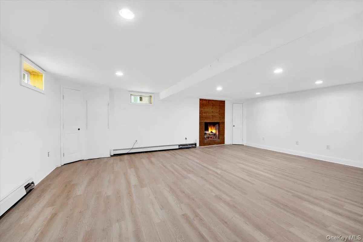 Basement area with light wood-style floors, a large fireplace, recessed lighting, a baseboard heating unit, and a baseboard radiator Basement area with light wood-style floors, a large fireplace, recessed lighting, a baseboard heating unit, and a baseboard radiator