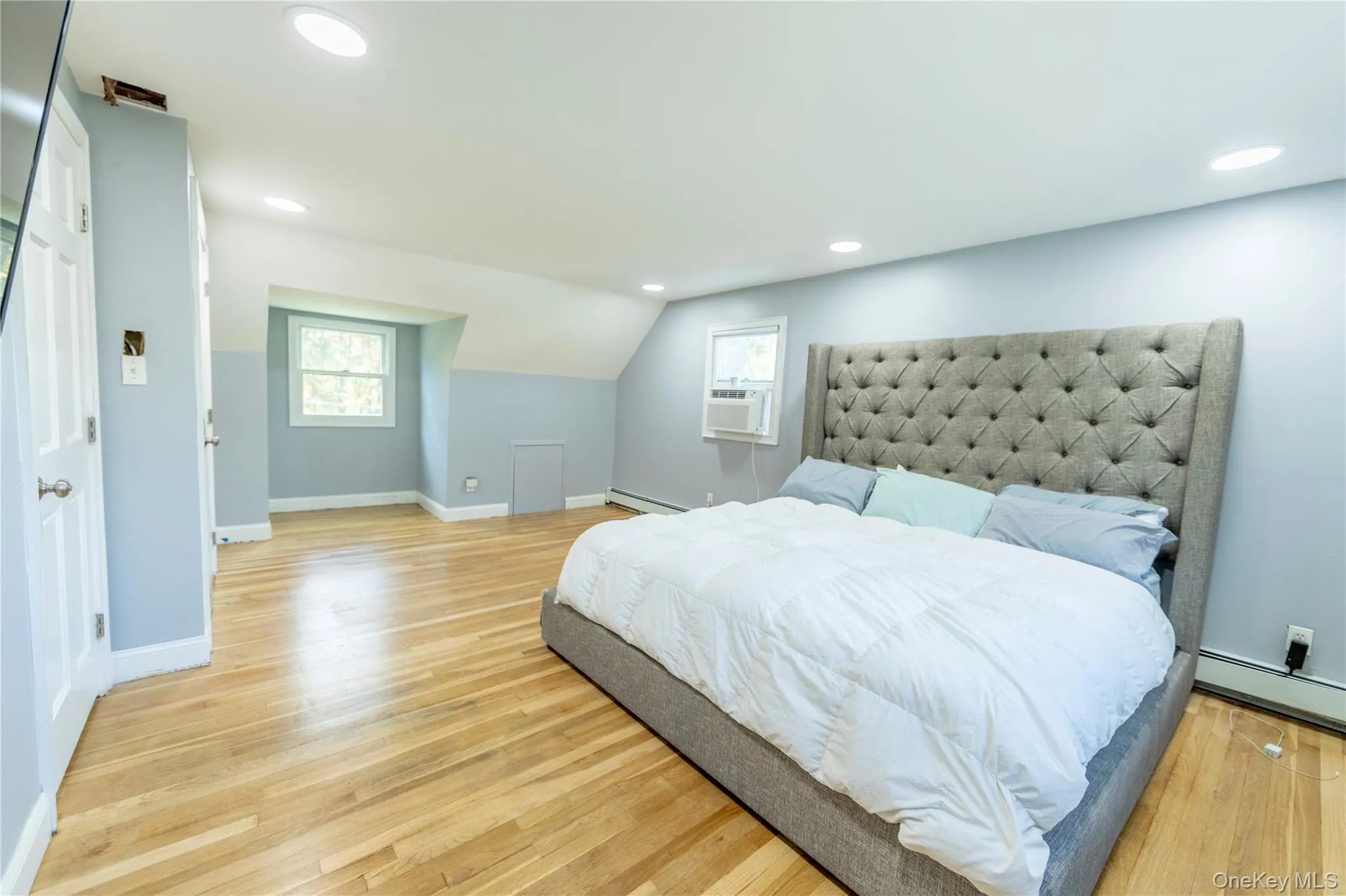 Primary Bedroom with light wood-style floors, multiple windows, recessed lighting, a baseboard radiator, and cooling unit Primary Bedroom with light wood-style floors, multiple windows, recessed lighting, a baseboard radiator, and cooling unit