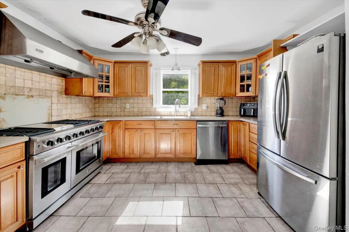 Kitchen featuring stainless steel appliances, glass insert cabinets, ventilation hood, and decorative backsplash Kitchen featuring stainless steel appliances, glass insert cabinets, ventilation hood, and decorative backsplash