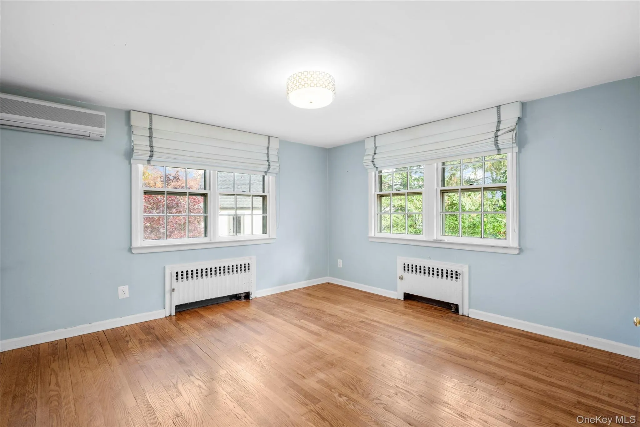Unfurnished room featuring healthy amount of natural light, radiator, and a wall unit AC Unfurnished room featuring healthy amount of natural light, radiator, and a wall unit AC