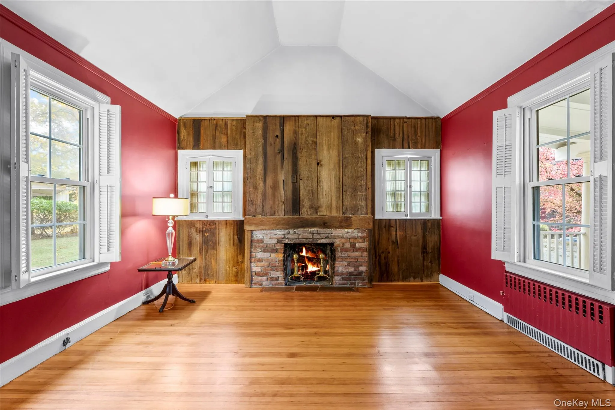 Sitting room with radiator, wood walls, a brick fireplace, hardwood / wood-style flooring, and lofted ceiling Sitting room with radiator, wood walls, a brick fireplace, hardwood / wood-style flooring, and lofted ceiling