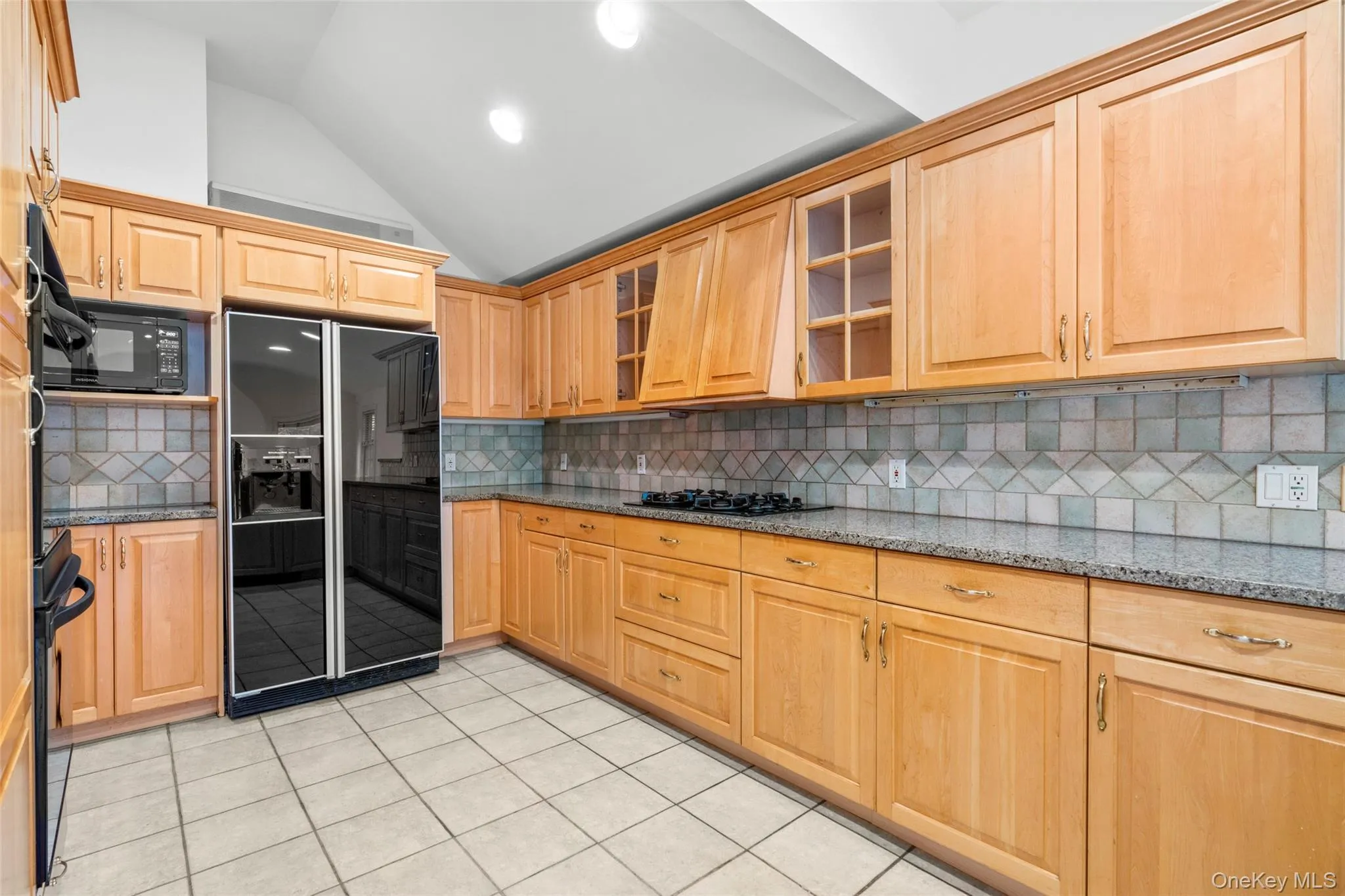 Kitchen with vaulted ceiling, dark stone counters, black appliances, light tile patterned flooring, and backsplash Kitchen with vaulted ceiling, dark stone counters, black appliances, light tile patterned flooring, and backsplash