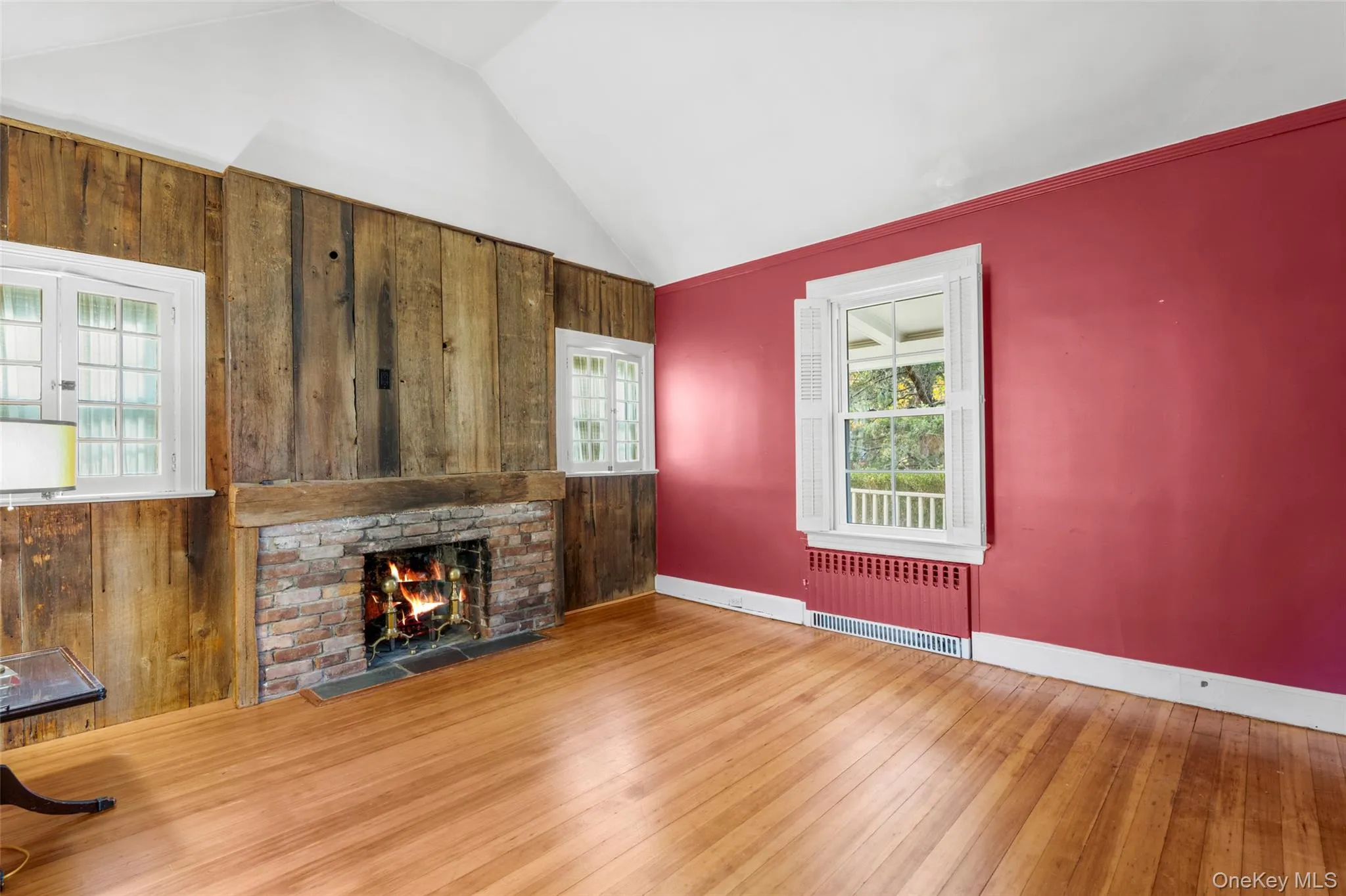 Unfurnished living room with wooden walls, a fireplace, radiator heating unit, wood finished floors, and high vaulted ceiling Unfurnished living room with wooden walls, a fireplace, radiator heating unit, wood finished floors, and high vaulted ceiling