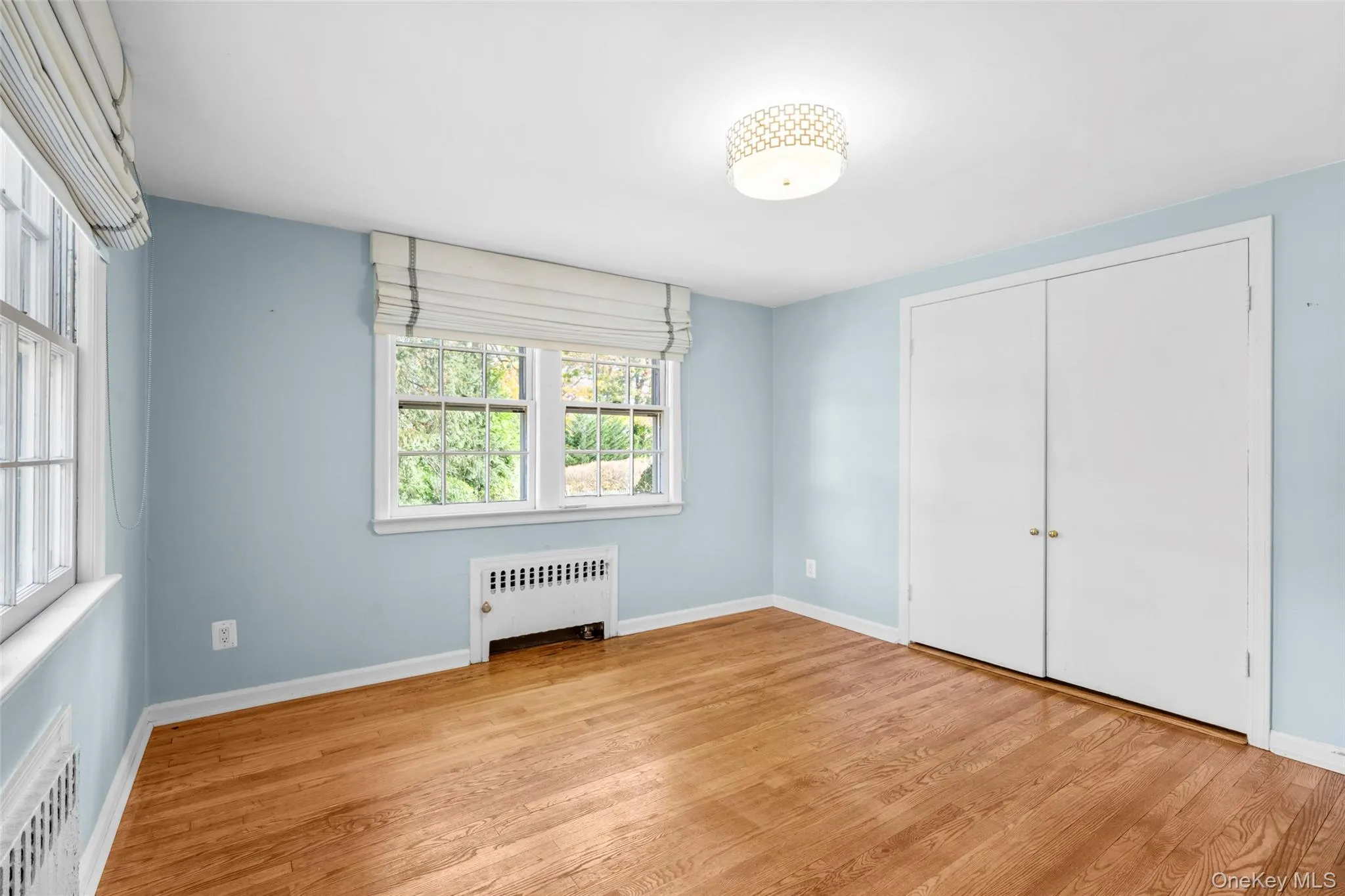Unfurnished bedroom featuring radiator heating unit, light wood finished floors, and a closet Unfurnished bedroom featuring radiator heating unit, light wood finished floors, and a closet