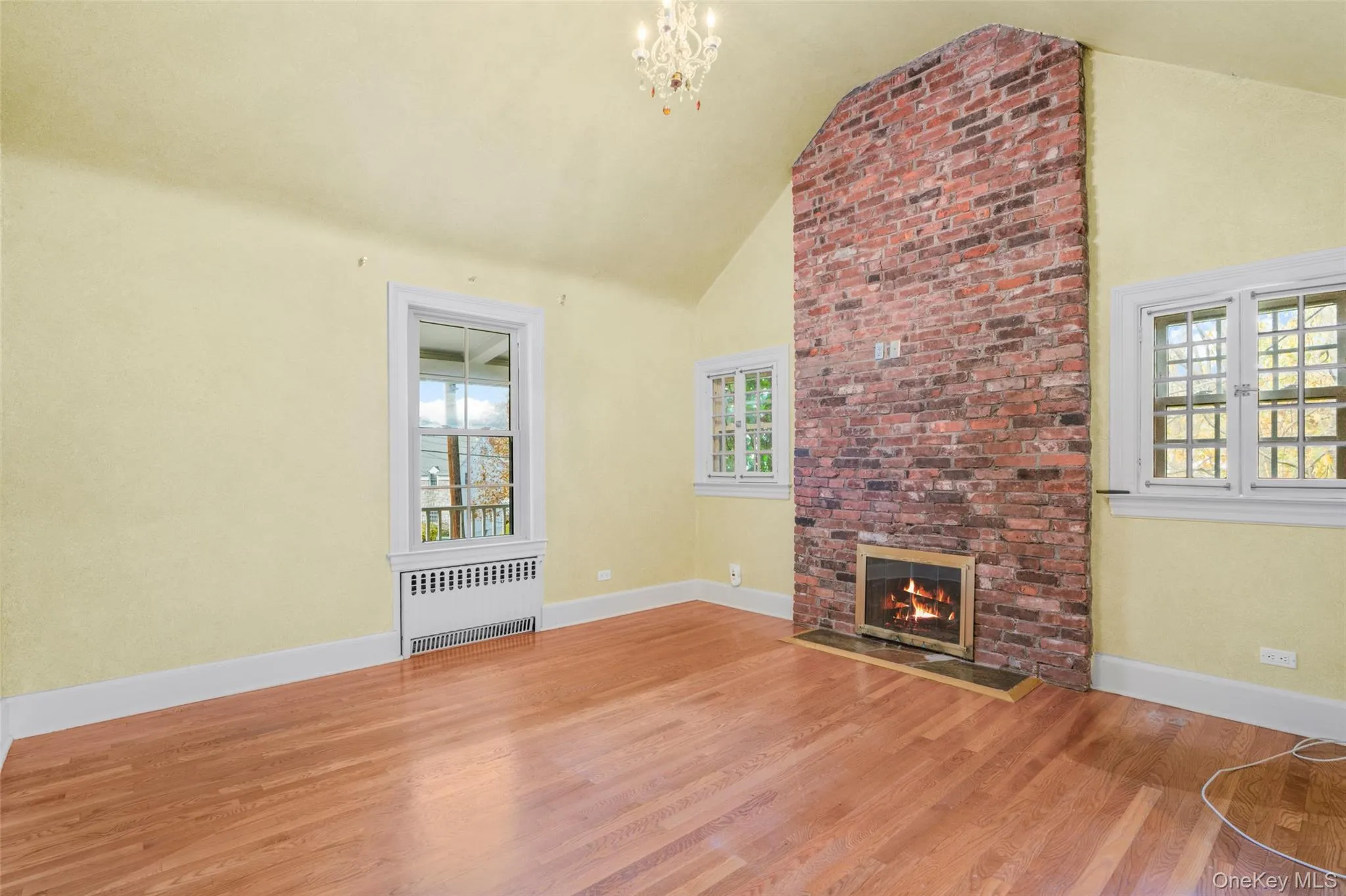Unfurnished living room with radiator heating unit, wood finished floors, high vaulted ceiling, a fireplace, and a chandelier Unfurnished living room with radiator heating unit, wood finished floors, high vaulted ceiling, a fireplace, and a chandelier
