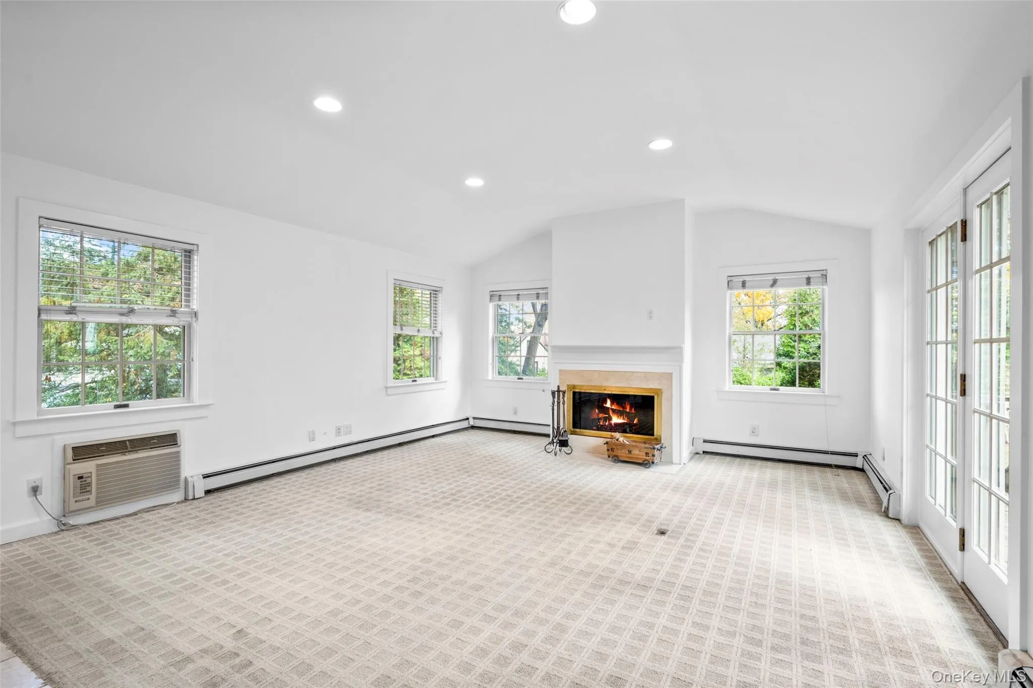 Unfurnished living room with healthy amount of natural light, recessed lighting, a glass covered fireplace, lofted ceiling, and light carpet Unfurnished living room with healthy amount of natural light, recessed lighting, a glass covered fireplace, lofted ceiling, and light carpet