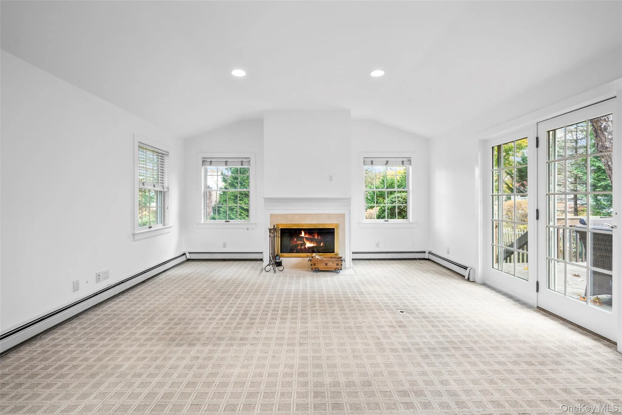 Unfurnished living room featuring healthy amount of natural light, a glass covered fireplace, recessed lighting, carpet, and vaulted ceiling Unfurnished living room featuring healthy amount of natural light, a glass covered fireplace, recessed lighting, carpet, and vaulted ceiling