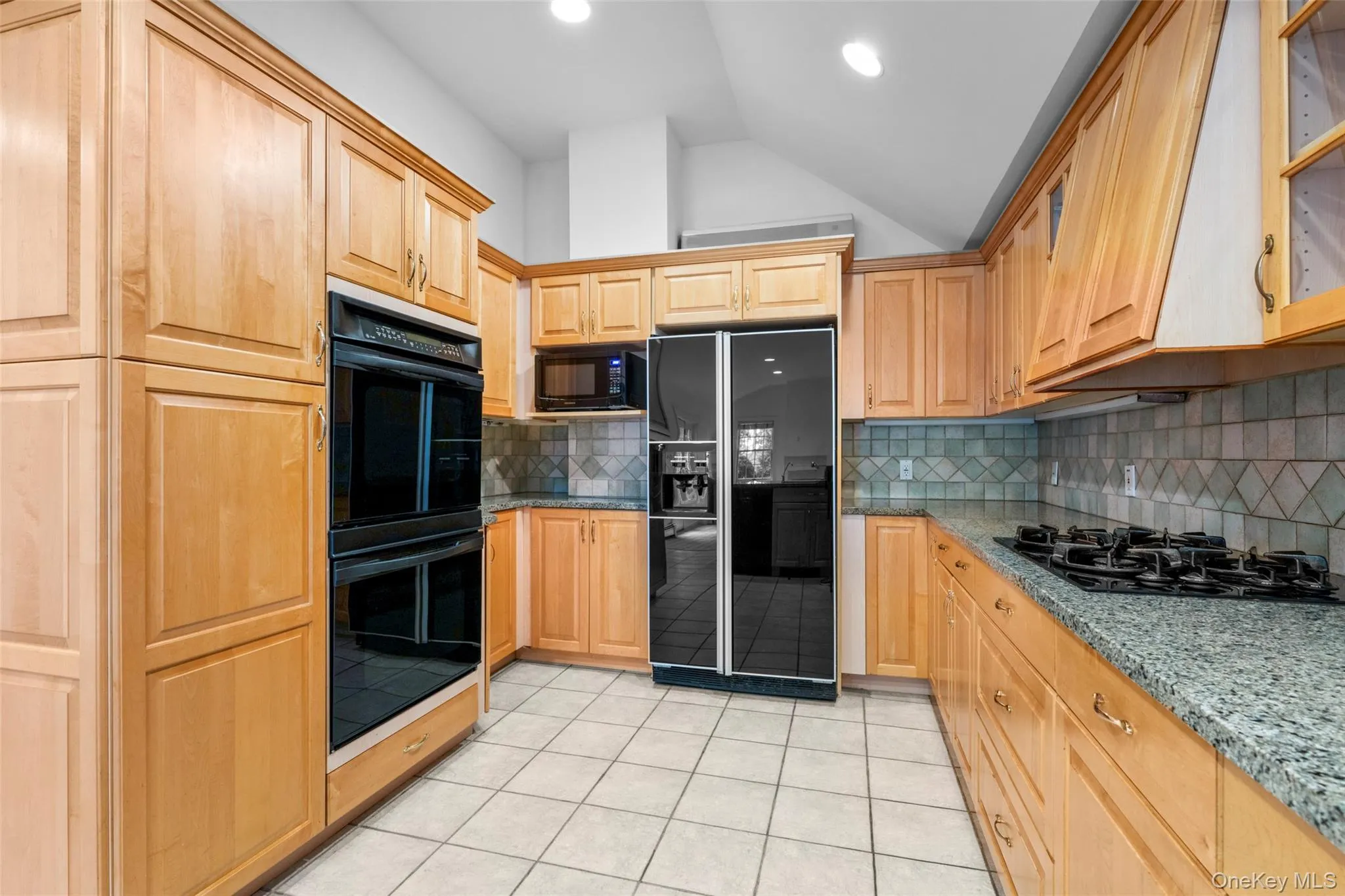 Kitchen featuring black appliances, light brown cabinets, light tile patterned floors, vaulted ceiling, and decorative backsplash Kitchen featuring black appliances, light brown cabinets, light tile patterned floors, vaulted ceiling, and decorative backsplash