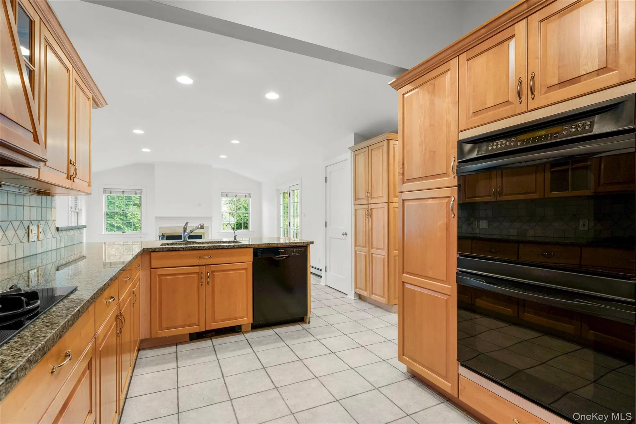 Kitchen with decorative backsplash, black appliances, recessed lighting, a peninsula, and dark stone countertops Kitchen with decorative backsplash, black appliances, recessed lighting, a peninsula, and dark stone countertops
