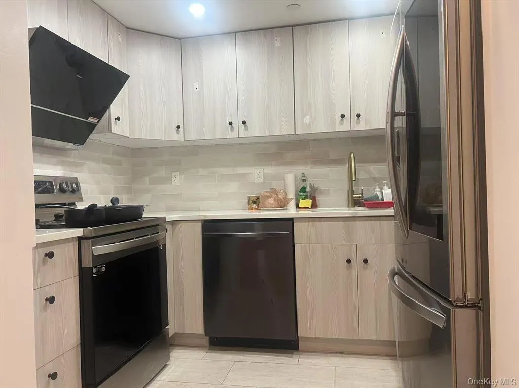 Kitchen with appliances with stainless steel finishes, extractor fan, backsplash, and light brown cabinetry Kitchen with appliances with stainless steel finishes, extractor fan, backsplash, and light brown cabinetry