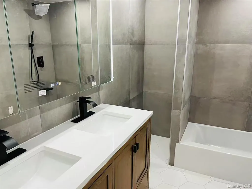 Full bathroom with tile walls, double vanity, and shower / washtub combination Full bathroom with tile walls, double vanity, and shower / washtub combination