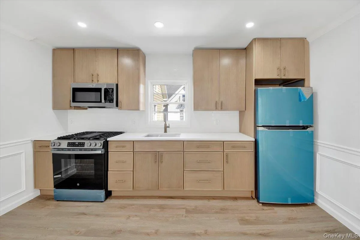 Kitchen with a wainscoted wall, a decorative wall, light brown cabinets, stainless steel appliances, and light countertops Kitchen with a wainscoted wall, a decorative wall, light brown cabinets, stainless steel appliances, and light countertops