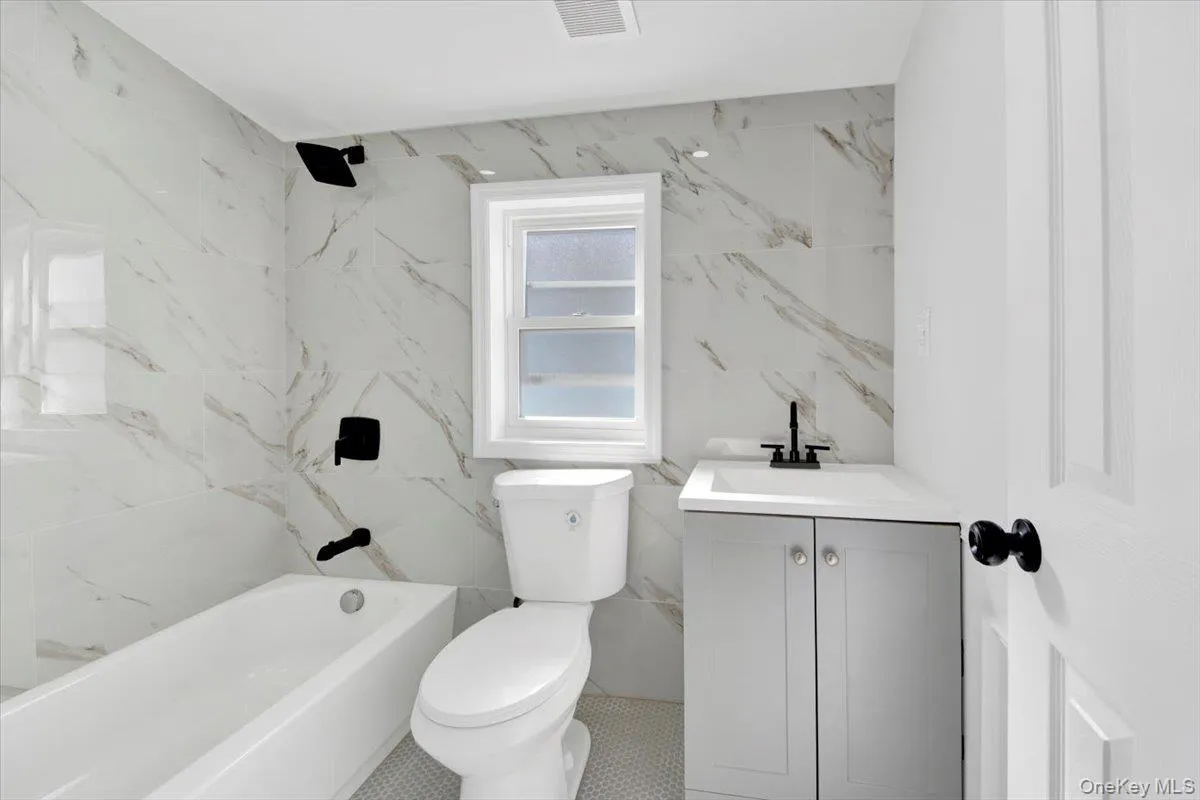 Bathroom with vanity, tile walls, and a combined bath / shower with marble appearance Bathroom with vanity, tile walls, and a combined bath / shower with marble appearance