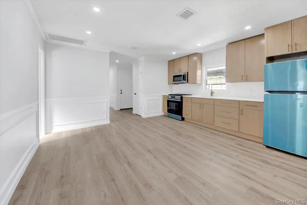 Kitchen featuring light brown cabinets, appliances with stainless steel finishes, wainscoting, light countertops, and a decorative wall Kitchen featuring light brown cabinets, appliances with stainless steel finishes, wainscoting, light countertops, and a decorative wall