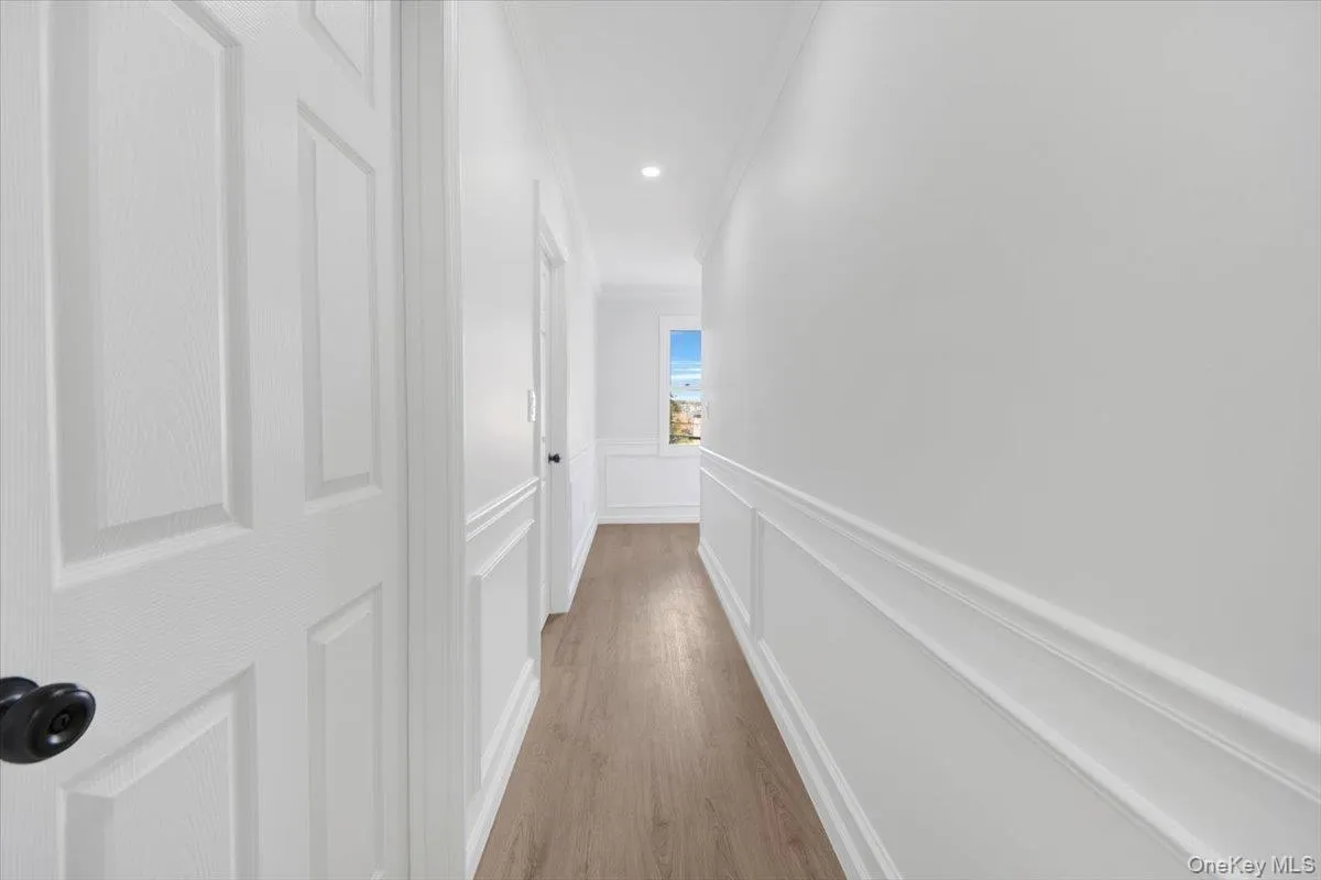 Hall featuring a decorative wall, a wainscoted wall, light wood-style floors, and crown molding Hall featuring a decorative wall, a wainscoted wall, light wood-style floors, and crown molding