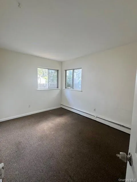 Spare room featuring a baseboard radiator and dark carpet Spare room featuring a baseboard radiator and dark carpet
