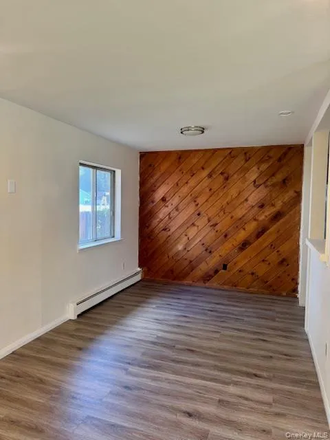 Unfurnished room with wood walls, baseboard heating, and wood finished floors Unfurnished room with wood walls, baseboard heating, and wood finished floors