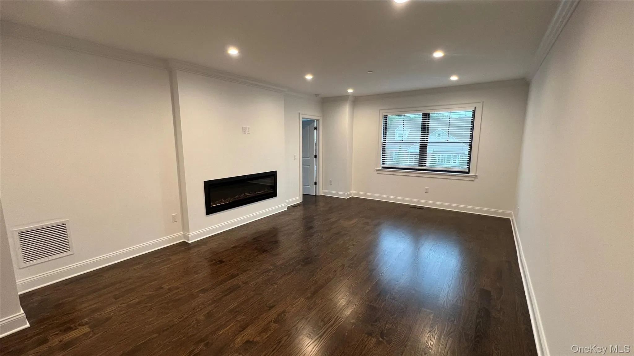 Unfurnished living room with ornamental molding, a glass covered fireplace, dark wood-style flooring, and recessed lighting Unfurnished living room with ornamental molding, a glass covered fireplace, dark wood-style flooring, and recessed lighting