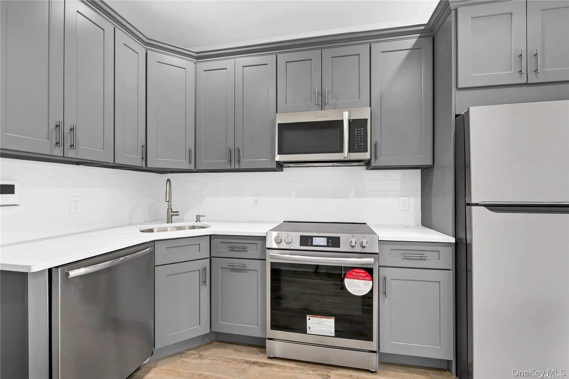 Kitchen with gray cabinets, stainless steel appliances, tasteful backsplash, light wood-type flooring, and light stone counters Kitchen with gray cabinets, stainless steel appliances, tasteful backsplash, light wood-type flooring, and light stone counters