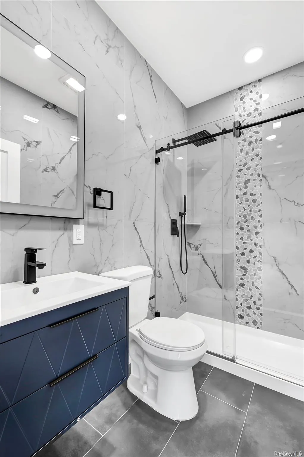 Full bathroom featuring tile walls, vanity, a marble finish shower, and dark tile patterned floors Full bathroom featuring tile walls, vanity, a marble finish shower, and dark tile patterned floors