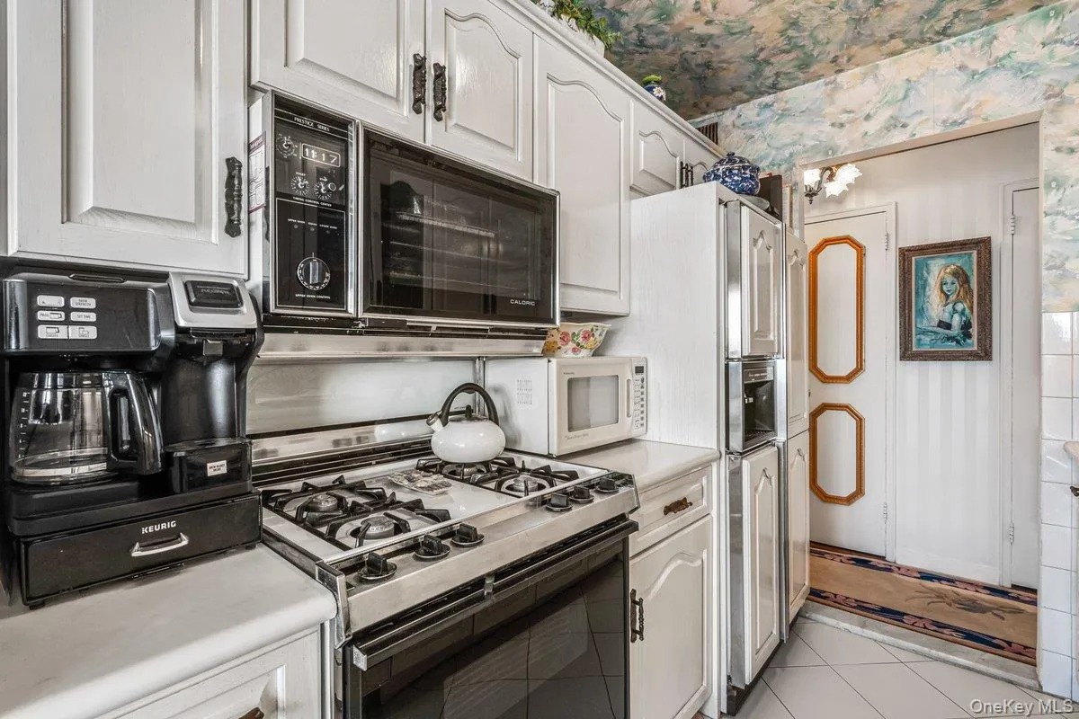 Kitchen with wallpapered walls, light tile patterned floors, light countertops, gas range oven, and white cabinets Kitchen with wallpapered walls, light tile patterned floors, light countertops, gas range oven, and white cabinets