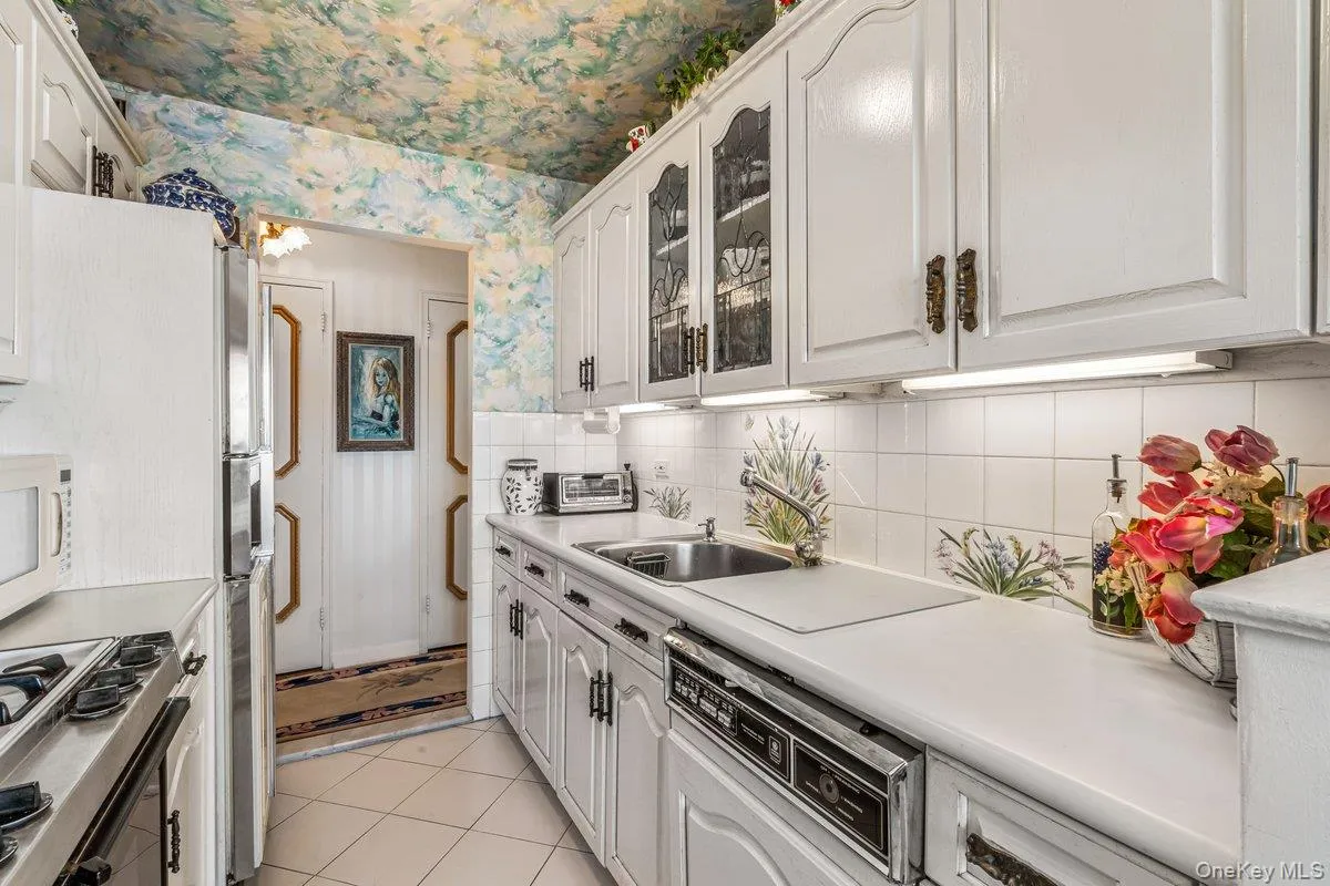 Kitchen with appliances with stainless steel finishes, light countertops, wallpapered walls, light tile patterned floors, and backsplash Kitchen with appliances with stainless steel finishes, light countertops, wallpapered walls, light tile patterned floors, and backsplash