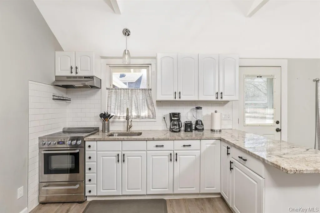 Kitchen with decorative backsplash, stainless steel range with electric cooktop, healthy amount of natural light, white cabinetry, and vaulted ceiling Kitchen with decorative backsplash, stainless steel range with electric cooktop, healthy amount of natural light, white cabinetry, and vaulted ceiling