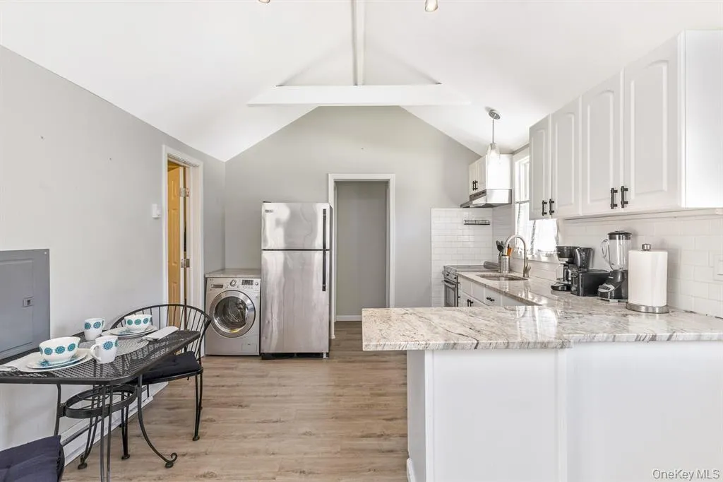 Kitchen featuring freestanding refrigerator, washer / clothes dryer, light wood-style flooring, a peninsula, and decorative backsplash Kitchen featuring freestanding refrigerator, washer / clothes dryer, light wood-style flooring, a peninsula, and decorative backsplash