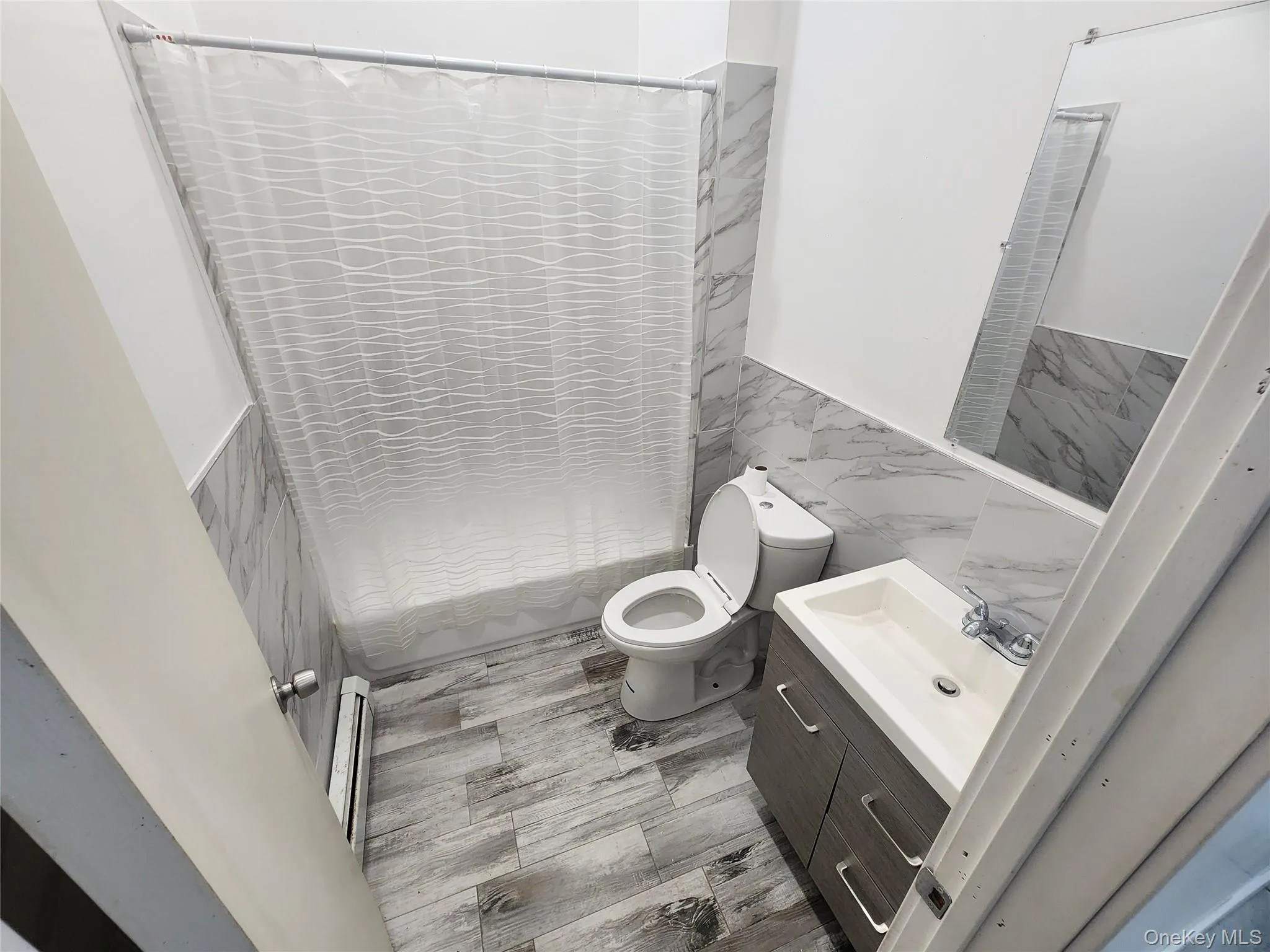 Full bathroom with tile walls, wainscoting, vanity, baseboard heating, and shower / tub combo Full bathroom with tile walls, wainscoting, vanity, baseboard heating, and shower / tub combo