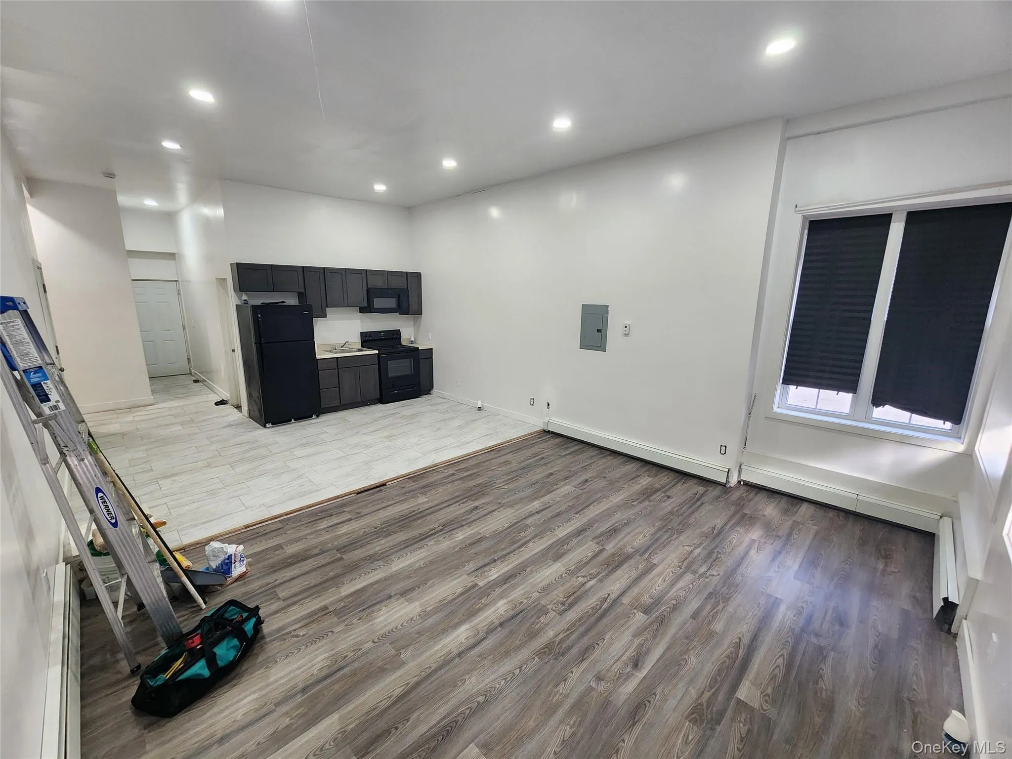 Unfurnished living room featuring wood finished floors, recessed lighting, electric panel, and a baseboard radiator Unfurnished living room featuring wood finished floors, recessed lighting, electric panel, and a baseboard radiator