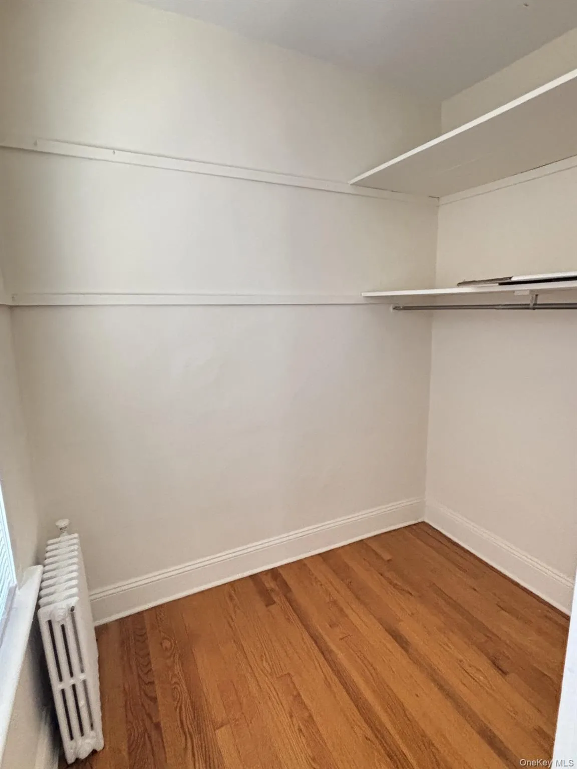 Walk in closet featuring radiator heating unit and wood finished floors Walk in closet featuring radiator heating unit and wood finished floors