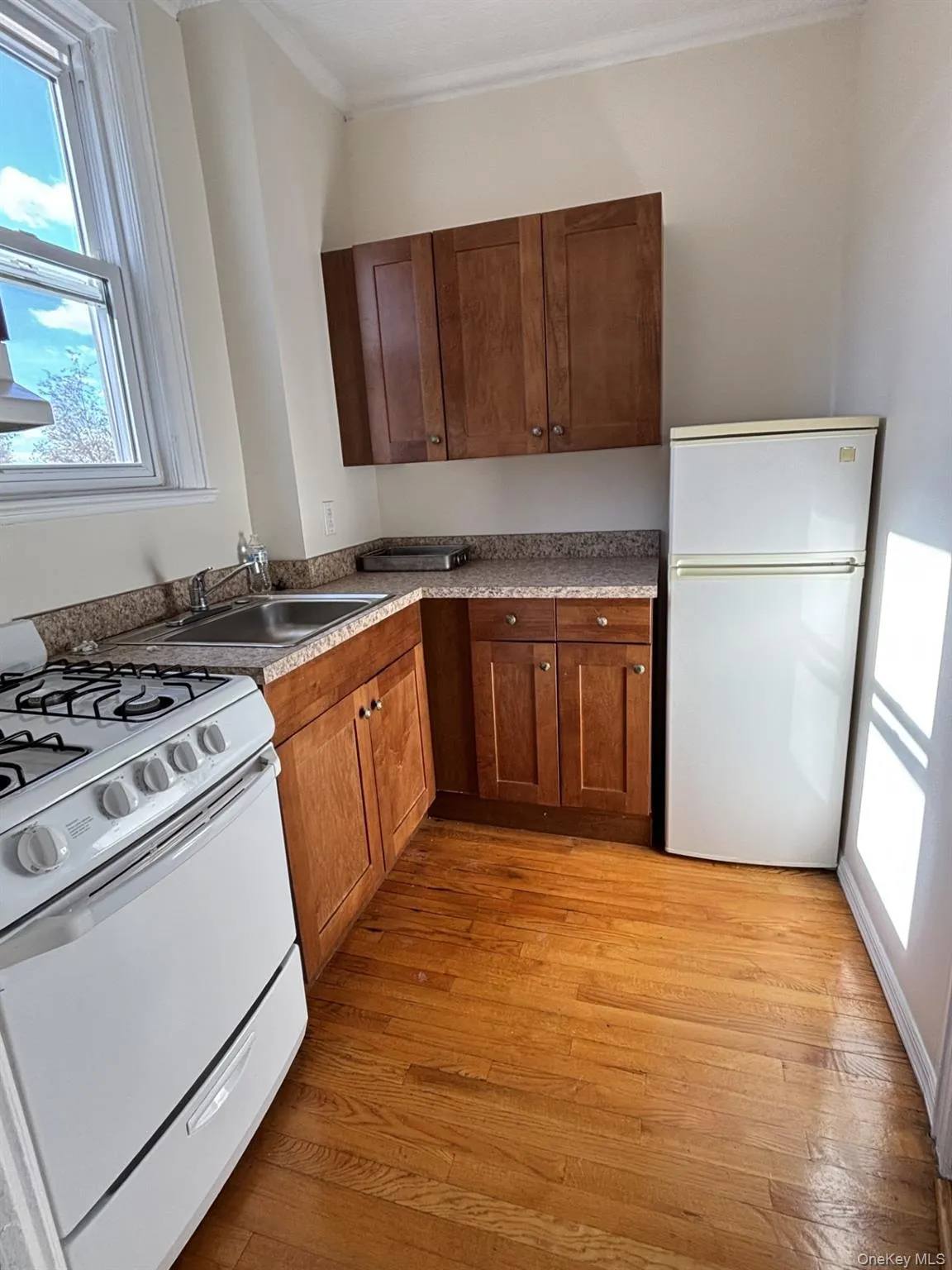Kitchen featuring white appliances, crown molding, light wood finished floors, and dark countertops Kitchen featuring white appliances, crown molding, light wood finished floors, and dark countertops