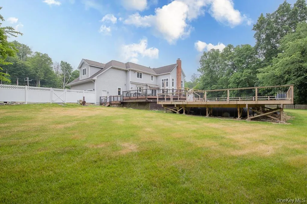Rear view of property with a deck, a fenced backyard, a chimney, view of wooded area, and stairs Rear view of property with a deck, a fenced backyard, a chimney, view of wooded area, and stairs
