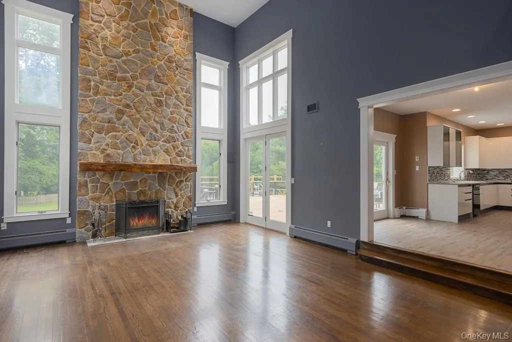 Unfurnished living room with dark wood finished floors, a towering ceiling, baseboard heating, and a stone fireplace Unfurnished living room with dark wood finished floors, a towering ceiling, baseboard heating, and a stone fireplace