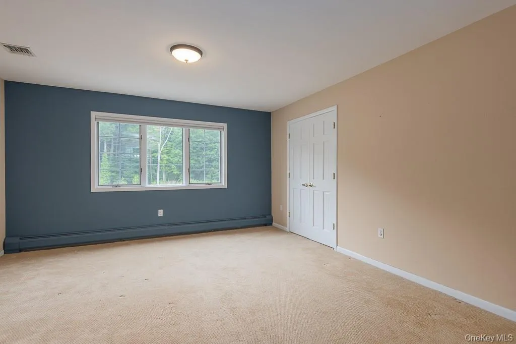 Unfurnished bedroom featuring light colored carpet and a baseboard radiator Unfurnished bedroom featuring light colored carpet and a baseboard radiator