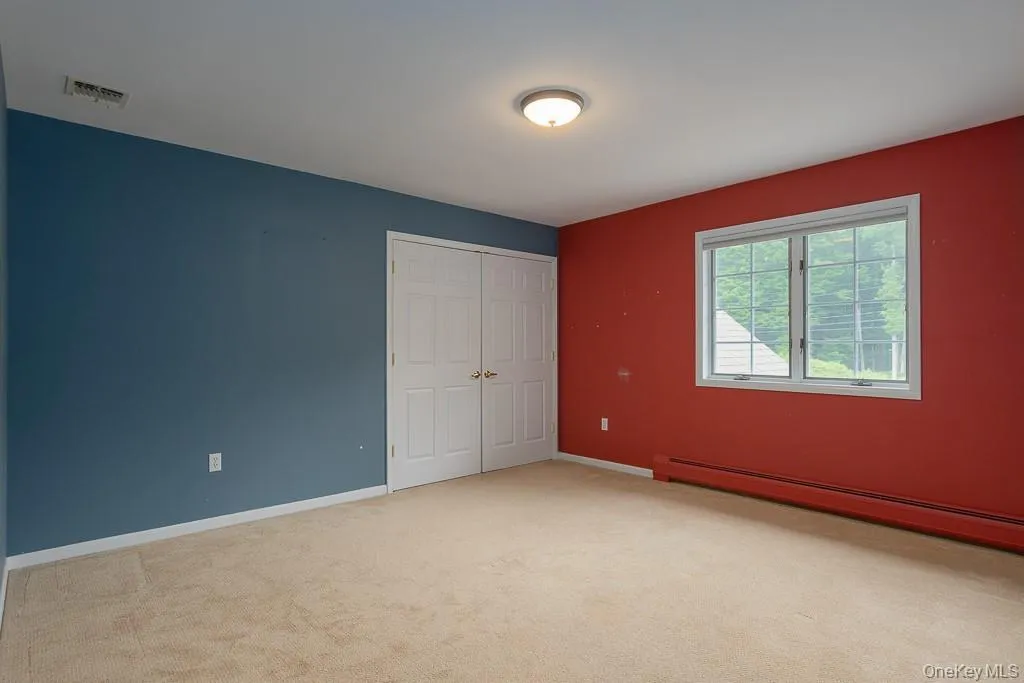 Unfurnished bedroom featuring a baseboard radiator, light colored carpet, and a closet Unfurnished bedroom featuring a baseboard radiator, light colored carpet, and a closet