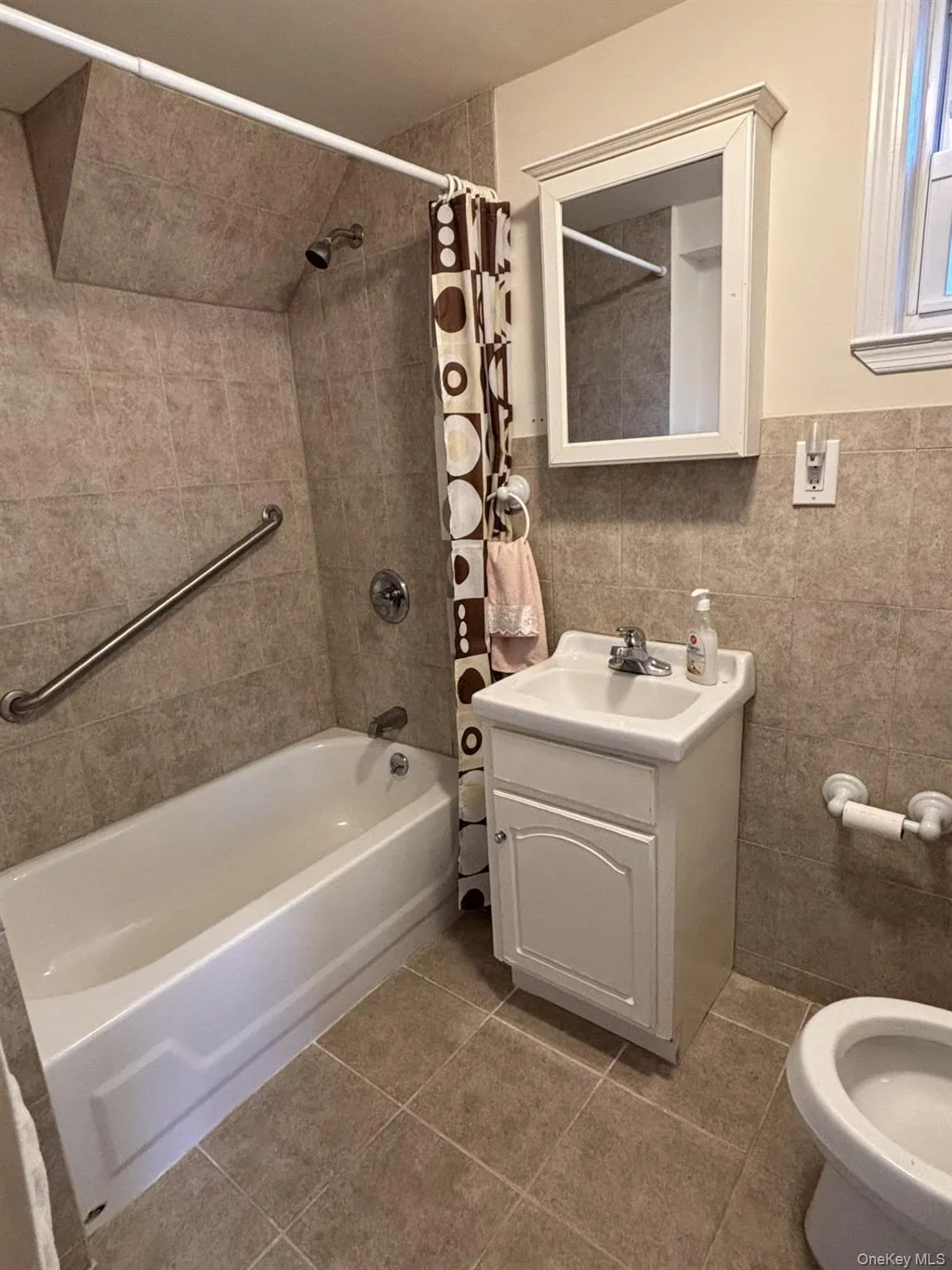 Full bath featuring shower / bath combination with curtain, tile walls, vanity, and light tile patterned floors Full bath featuring shower / bath combination with curtain, tile walls, vanity, and light tile patterned floors