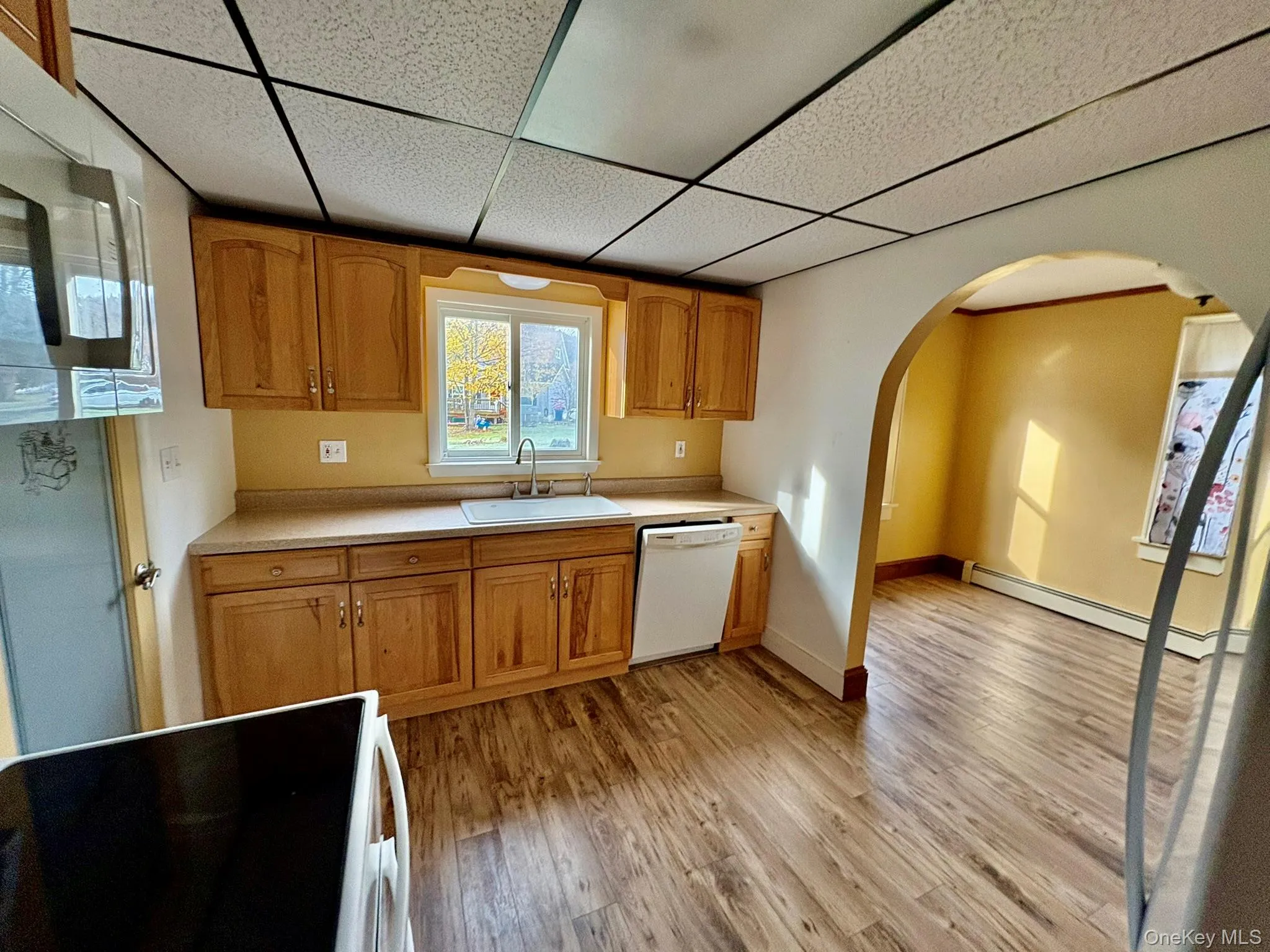 Kitchen with white appliances, light countertops, baseboard heating, arched walkways, and light wood finished floors Kitchen with white appliances, light countertops, baseboard heating, arched walkways, and light wood finished floors