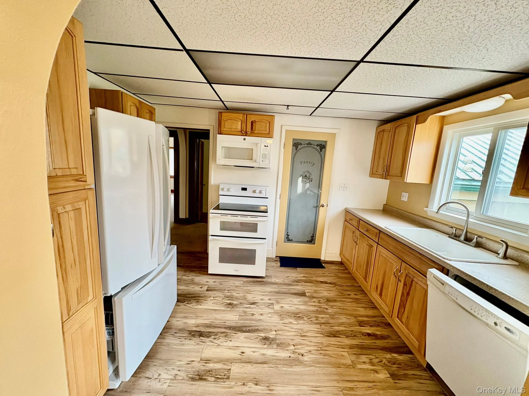 Kitchen featuring white appliances, light wood-style flooring, light countertops, and a paneled ceiling Kitchen featuring white appliances, light wood-style flooring, light countertops, and a paneled ceiling
