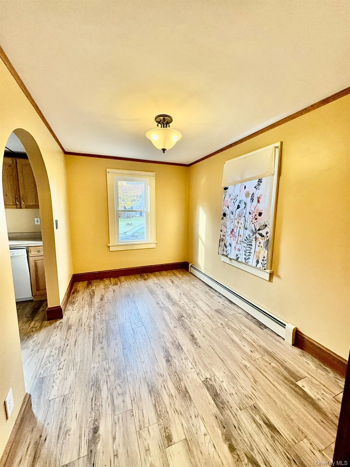 Spare room with arched walkways, a baseboard heating unit, light wood finished floors, and crown molding Spare room with arched walkways, a baseboard heating unit, light wood finished floors, and crown molding