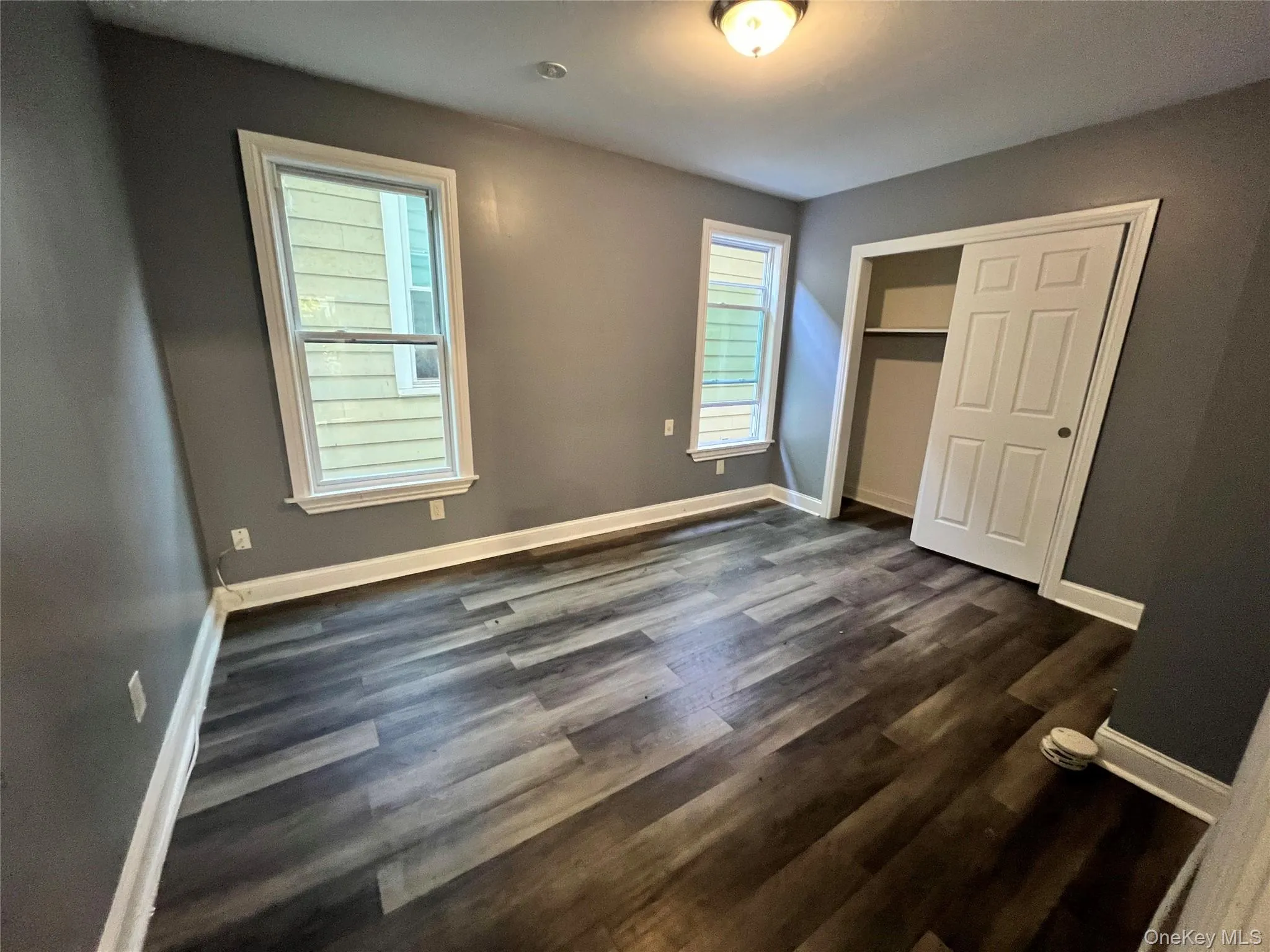 Unfurnished bedroom with a closet, dark wood-type flooring, and multiple windows Unfurnished bedroom with a closet, dark wood-type flooring, and multiple windows