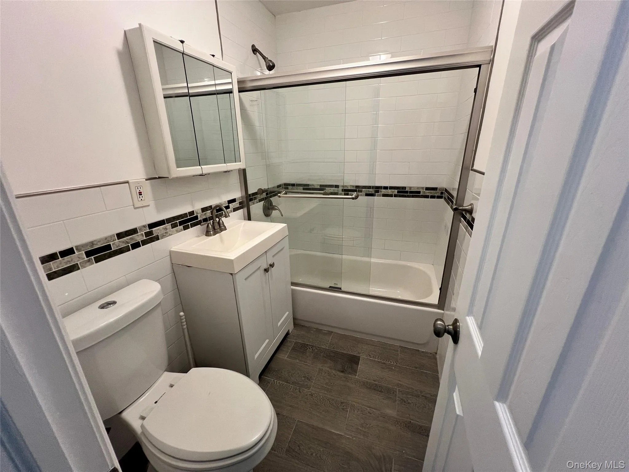 Full bathroom with vanity, enclosed tub / shower combo, wood tiled floors, and tile walls Full bathroom with vanity, enclosed tub / shower combo, wood tiled floors, and tile walls