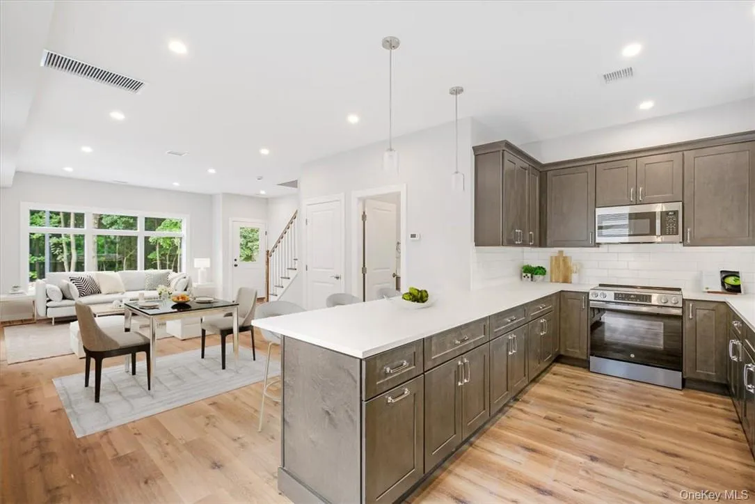 View from Kitchen into Dining area and Living Room*Virtually Staged. Kitchen featuring light wood-type flooring, kitchen peninsula, appliances with stainless steel finishes, and hanging light fixtures *Virtually Staged View from Kitchen into Dining area and Living Room*Virtually Staged. Kitchen featuring light wood-type flooring, kitchen peninsula, appliances with stainless steel finishes, and hanging light fixtures *Virtually Staged