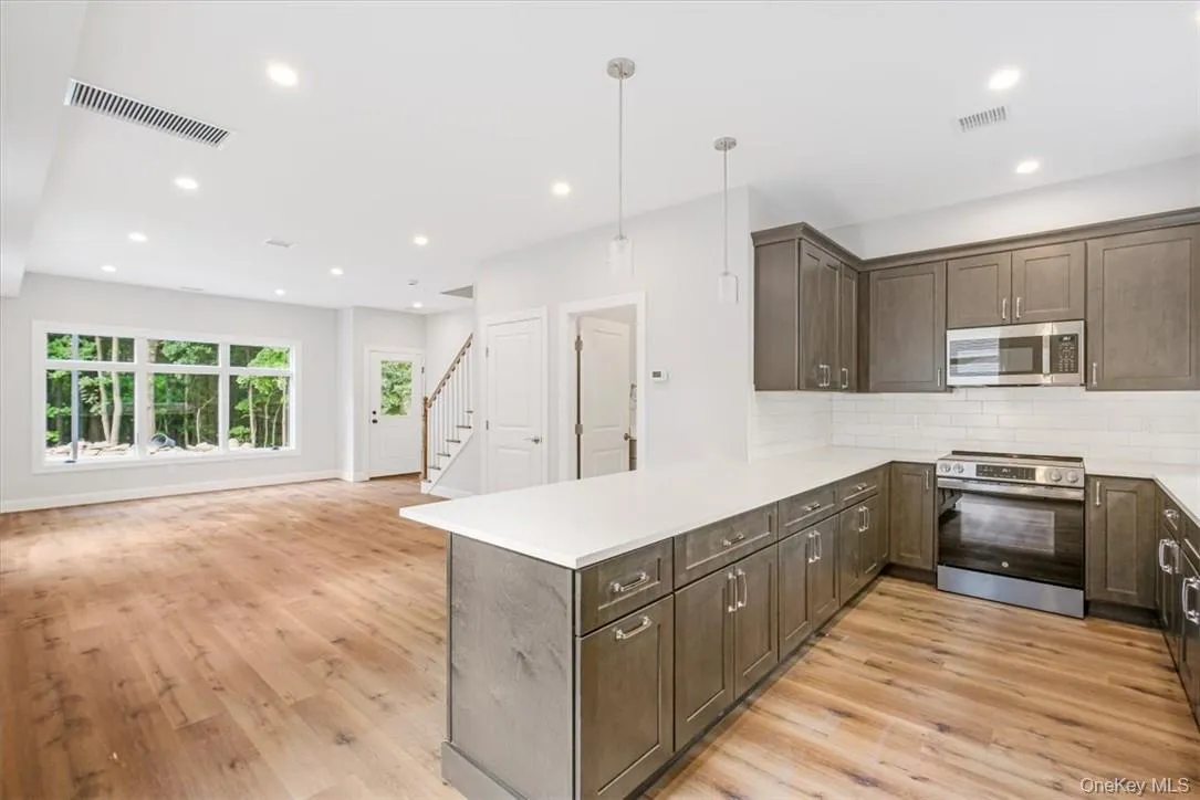 Kitchen featuring light wood-type flooring, kitchen peninsula, appliances with stainless steel finishes, and hanging light fixtures Kitchen featuring light wood-type flooring, kitchen peninsula, appliances with stainless steel finishes, and hanging light fixtures