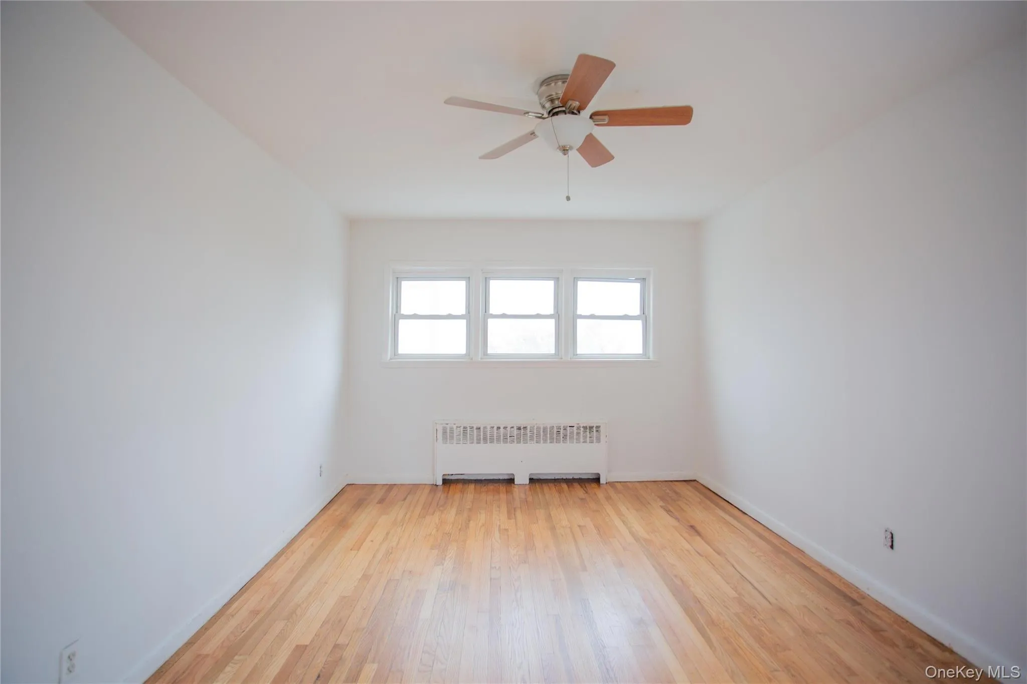 Spare room featuring radiator heating unit, light wood-type flooring, and a ceiling fan Spare room featuring radiator heating unit, light wood-type flooring, and a ceiling fan
