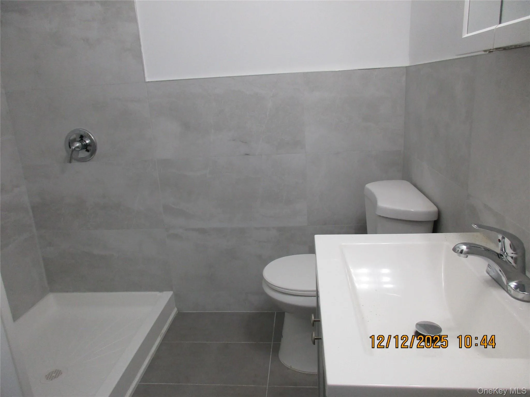 Bathroom featuring tile walls, a shower stall, dark tile patterned flooring, and vanity Bathroom featuring tile walls, a shower stall, dark tile patterned flooring, and vanity