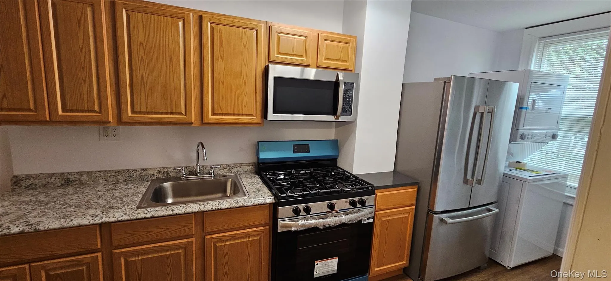 Kitchen featuring stainless steel appliances, washer / clothes dryer, brown cabinetry, and dark wood-type flooring Kitchen featuring stainless steel appliances, washer / clothes dryer, brown cabinetry, and dark wood-type flooring