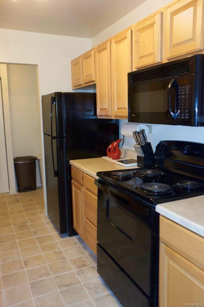 Kitchen with black appliances, light countertops, light tile patterned flooring, and light brown cabinets Kitchen with black appliances, light countertops, light tile patterned flooring, and light brown cabinets